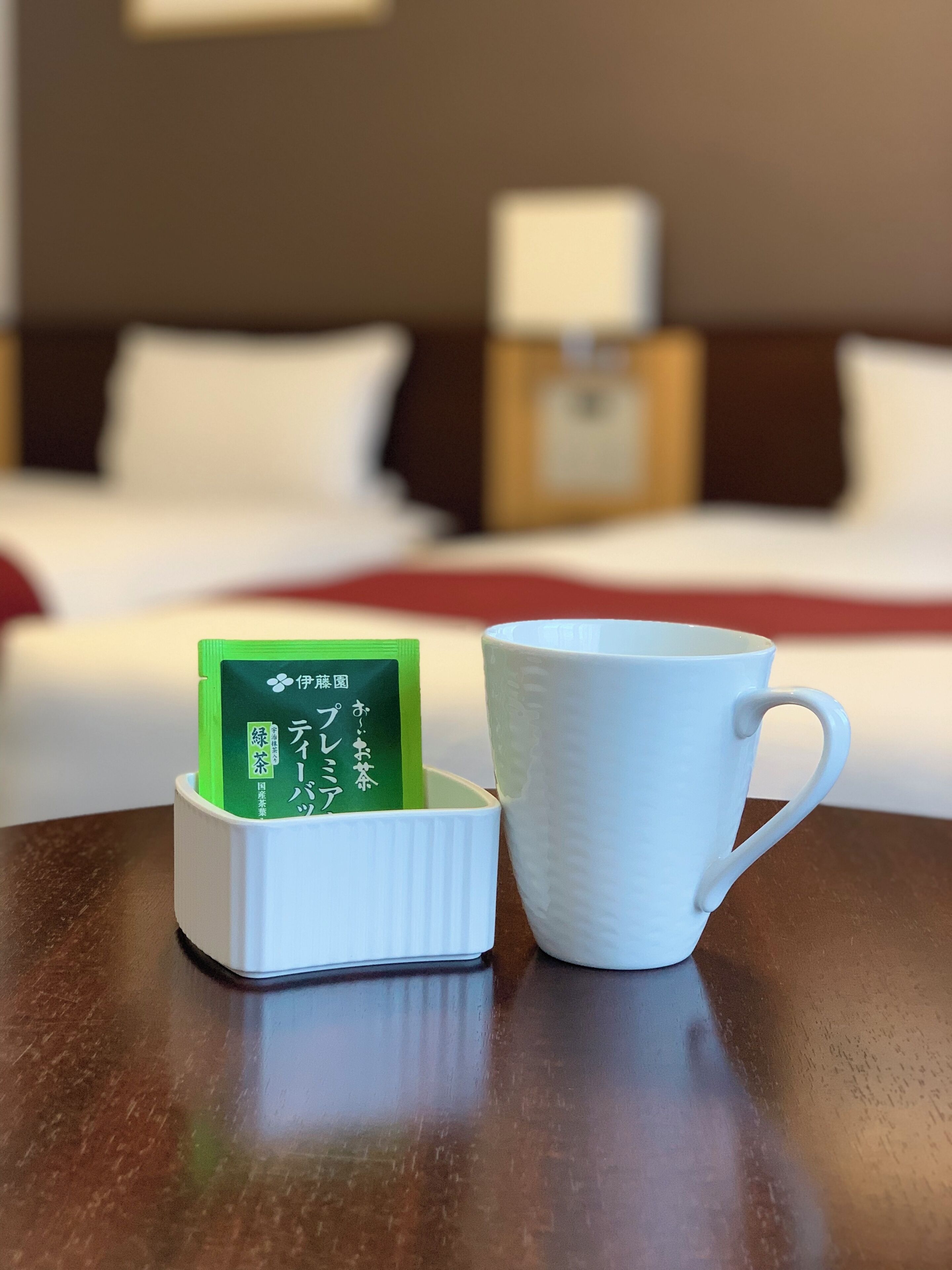 Una taza blanca y un sobre de té verde sobre una mesa de madera en una habitación de hotel.