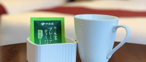 Una taza blanca y un sobre de té verde sobre una mesa de madera en una habitación de hotel.