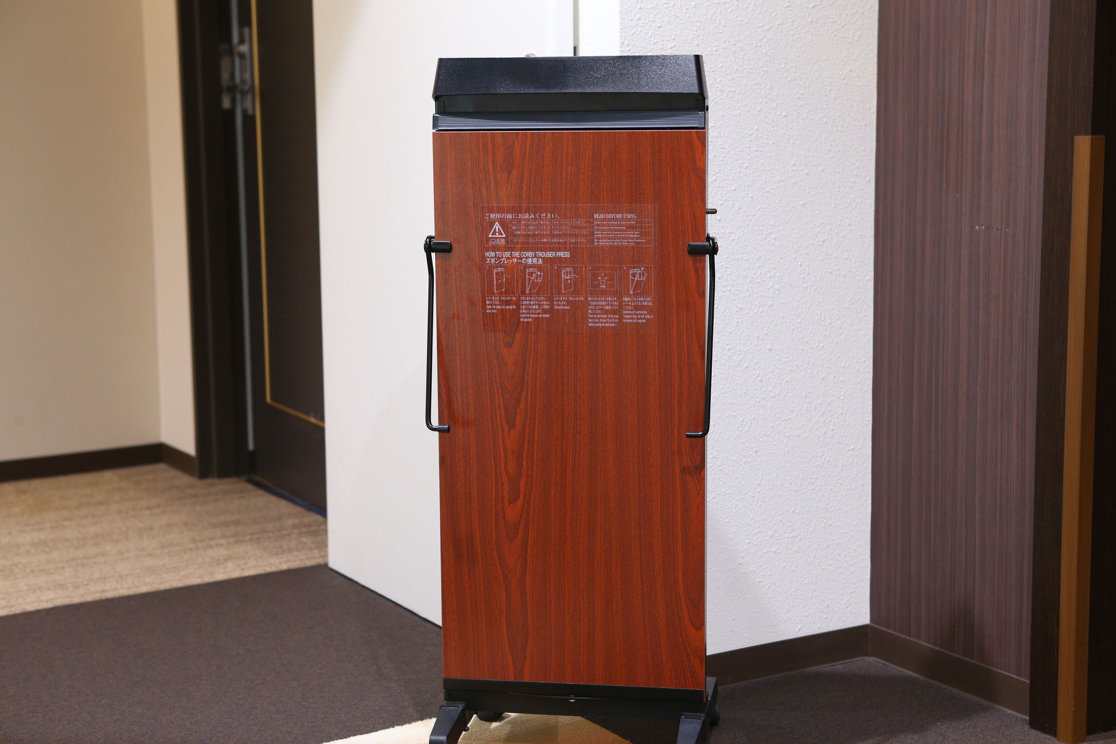 Ein Holzkorpus mit schwarzer Ablage und zwei schwarzen Griffen, mit Warnhinweisen und Anleitungen.