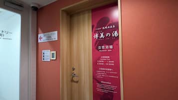 Un mur rouge avec une porte en bois, une enseigne indiquant un spa pour femmes et une autre pour des services de blanchisserie.