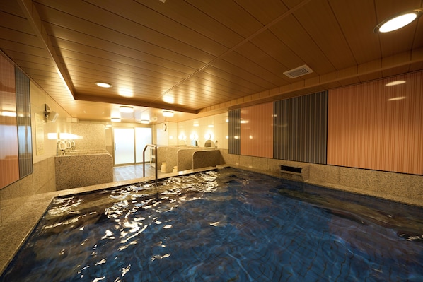 Una piscina interior con suelo de baldosas, un vestuario con ducha y techo de madera.