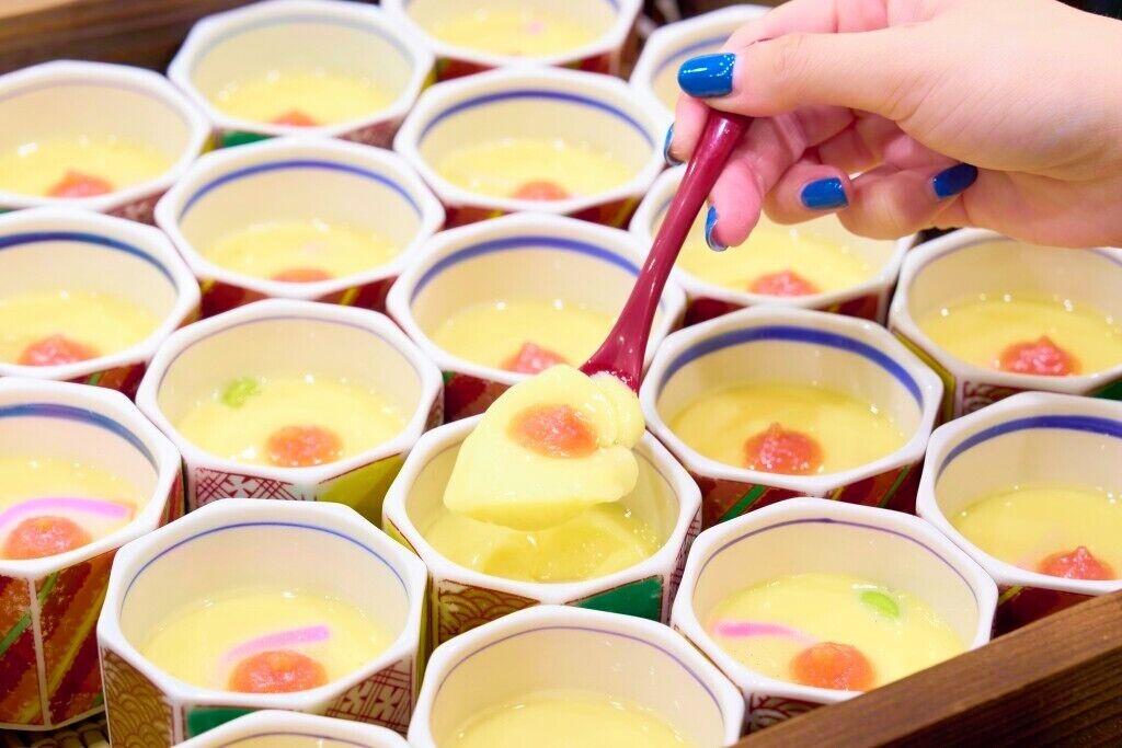 A tray of small cups with a yellowish liquid and a slice of fruit on top.