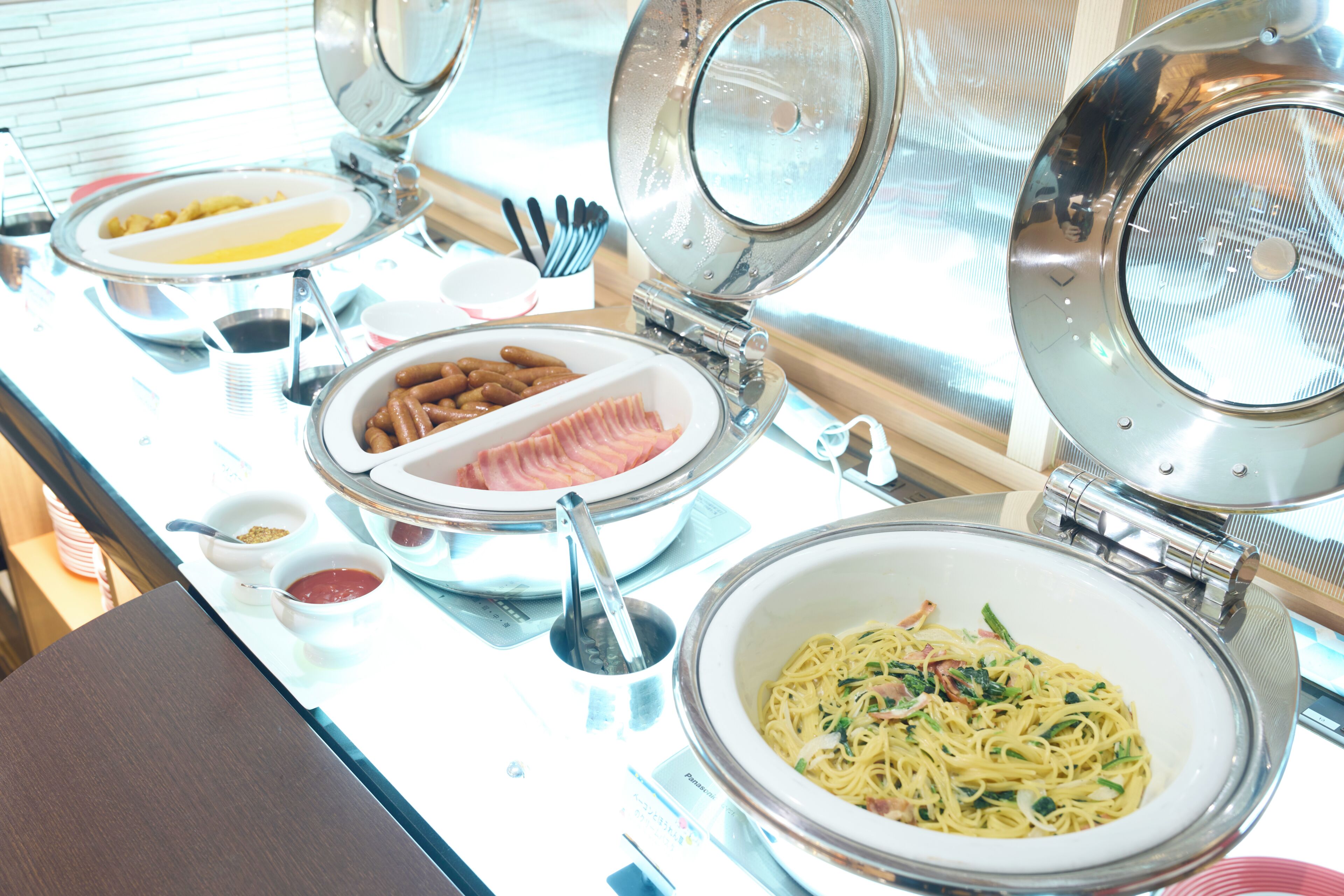 A buffet setup with various dishes including pasta, sausages, and a bowl of soup.