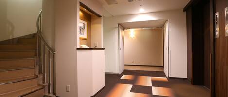 A hotel hallway with a staircase, a reception desk, and a door leading to another room.