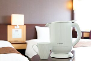 A white electric kettle and a white mug on a table in a hotel room.
