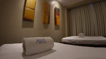 Une chambre d’hôtel avec un lit parfaitement fait, une serviette blanche roulée sur laquelle on peut lire « salle de sport Azure », et deux tableaux abstraits accrochés au mur.