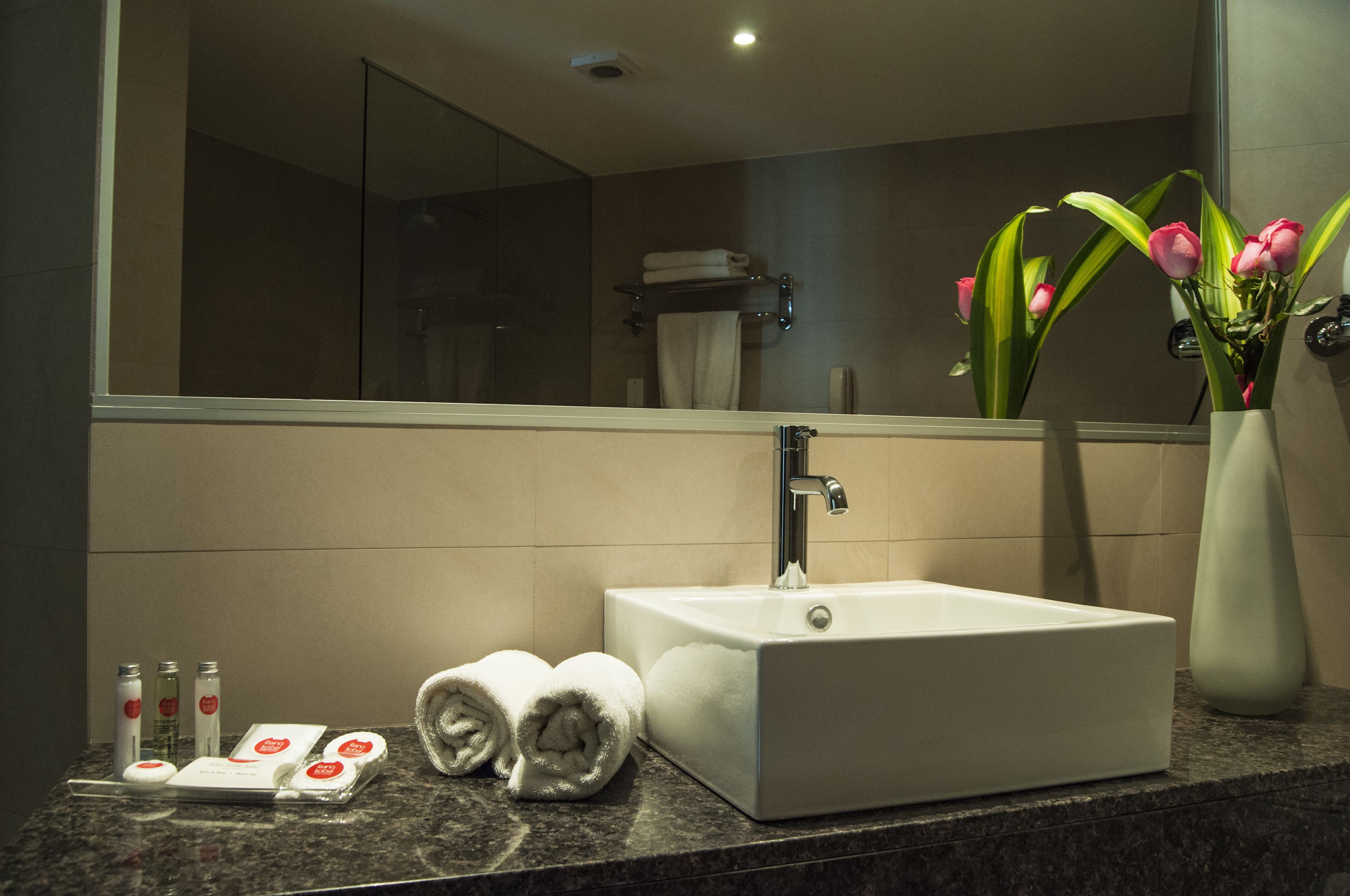 A bathroom with a white sink, a mirror, a towel rack, and a vase with flowers.
