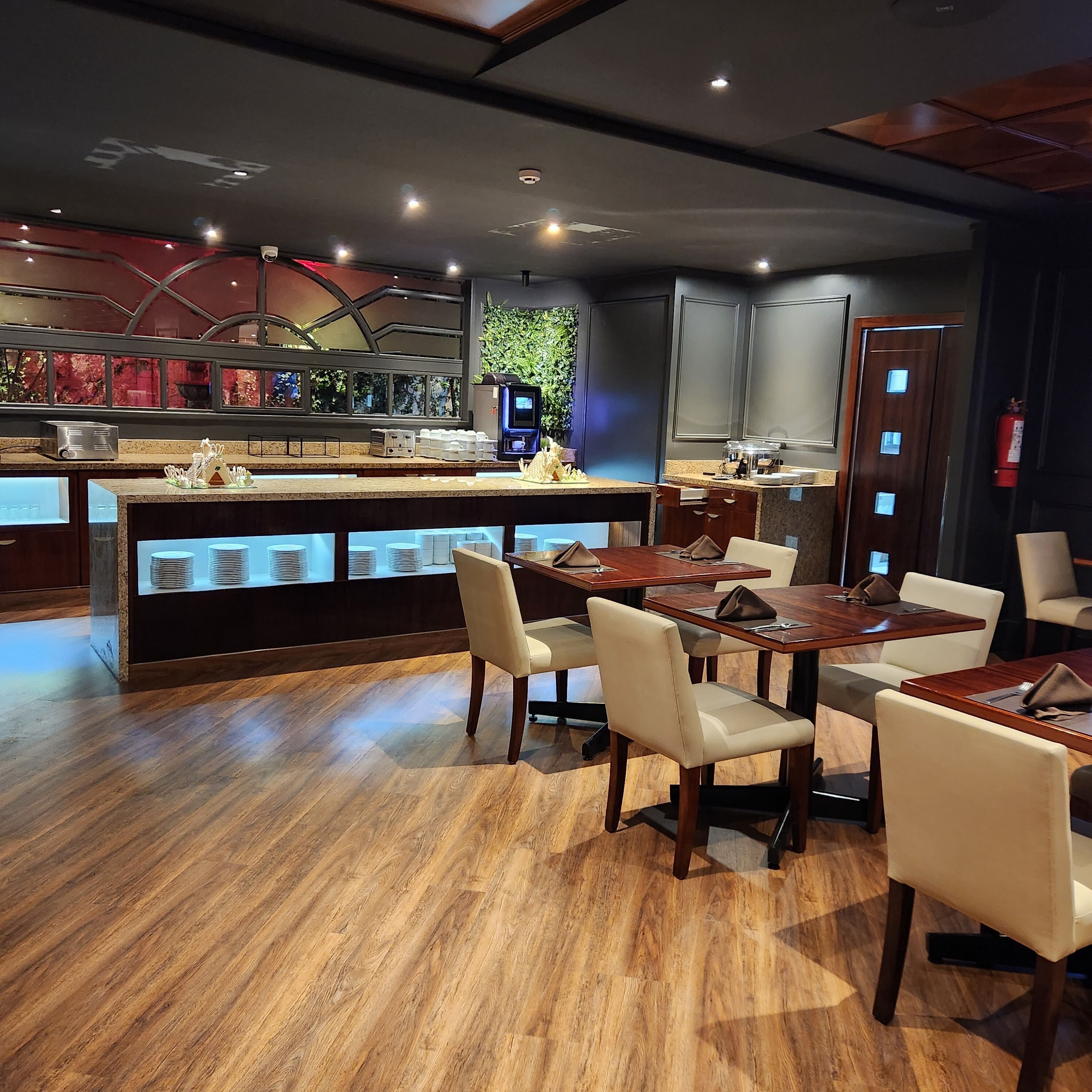 A restaurant with wooden flooring, a central bar area, and a seating arrangement with tables and chairs.