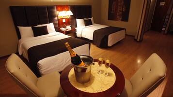 A hotel room with two beds, a nightstand with lamps, a table with a bottle of champagne and glasses, and a wooden floor.
