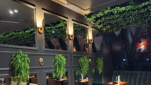 Un restaurante con paredes oscuras, paneles espejados y plantas verdes.