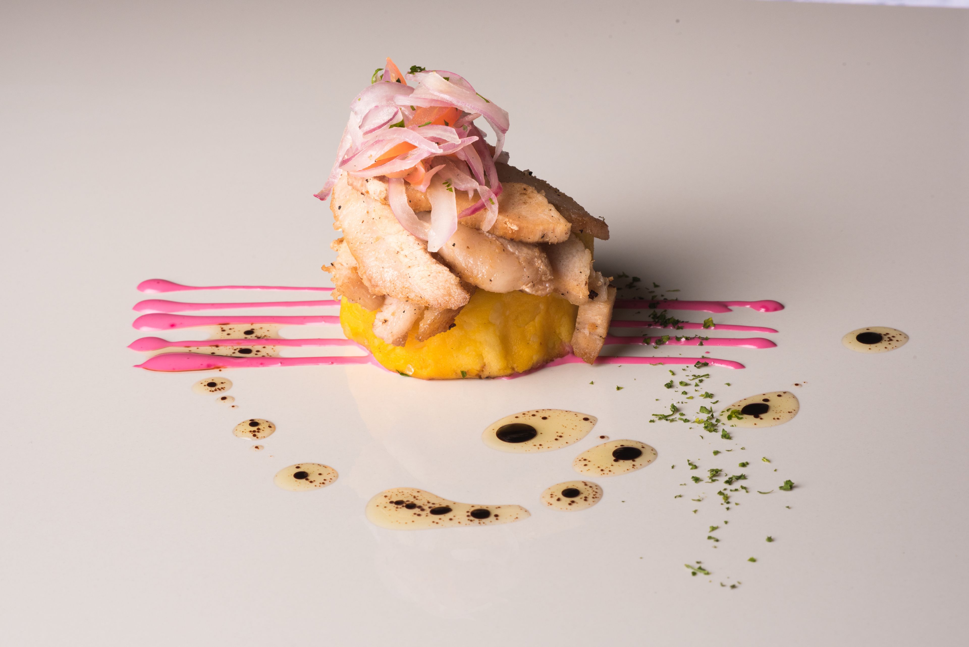 Een gerecht met een gele basis, roze saus, en versierde uien en kruiden.