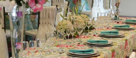 A long dining table set with floral tablecloth, glassware, and folded napkins.