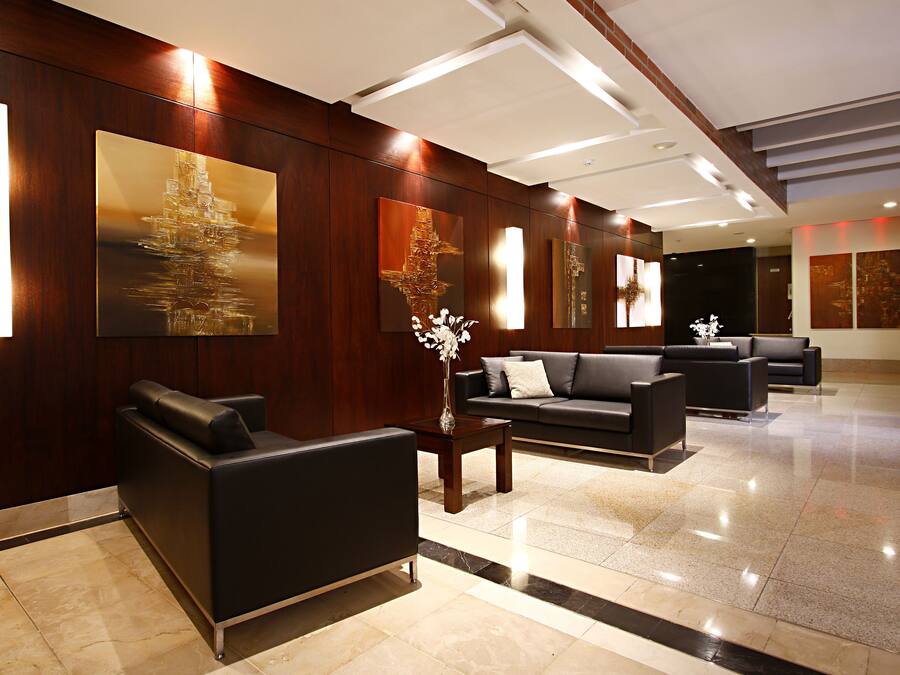 A modern lobby with dark wood paneling, a black leather sofa, a coffee table, and a vase with white flowers.