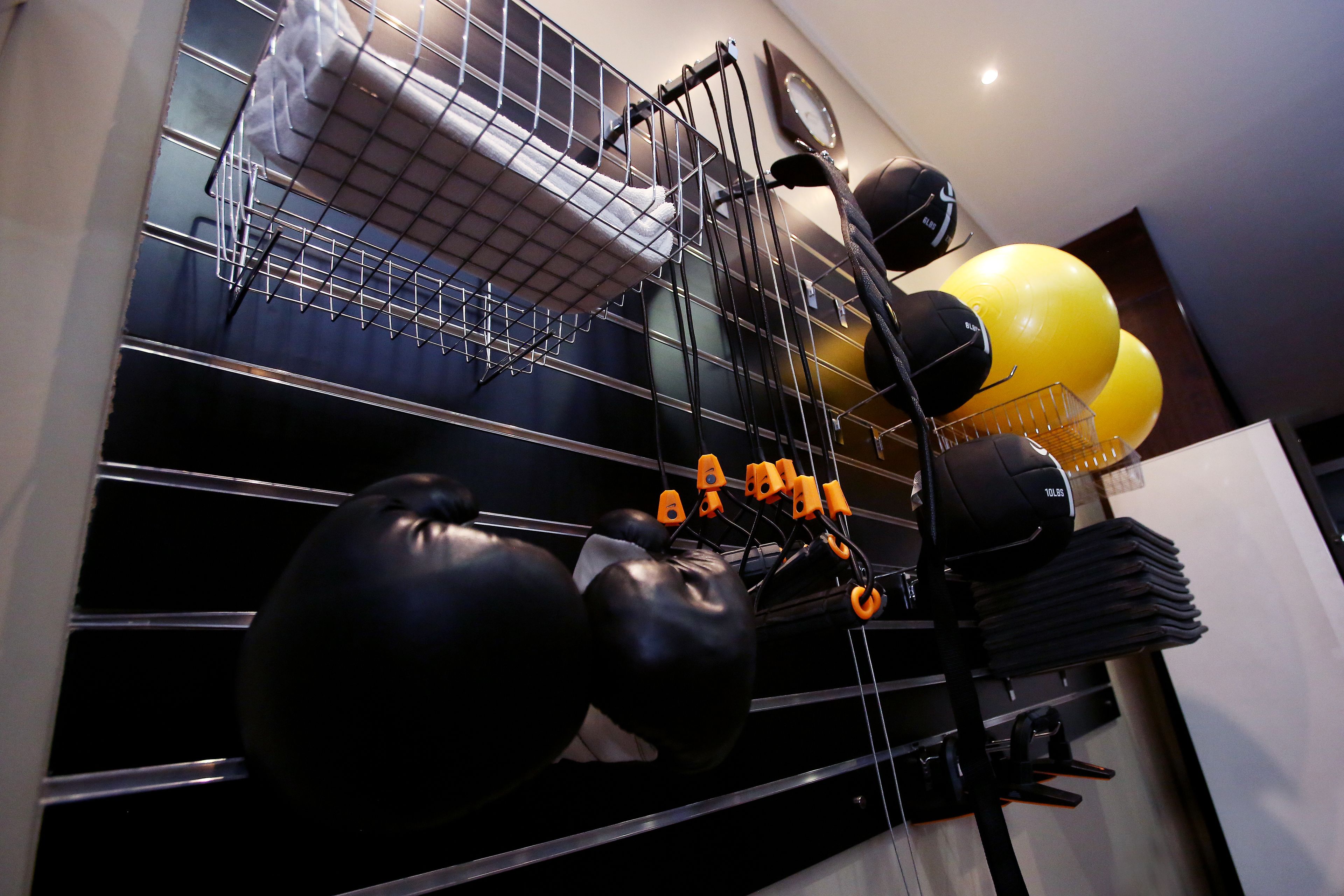 Een sportschool met fitnessapparatuur, waaronder zwarte en gele trainingsballen, en een rek met opgevouwen matten.
