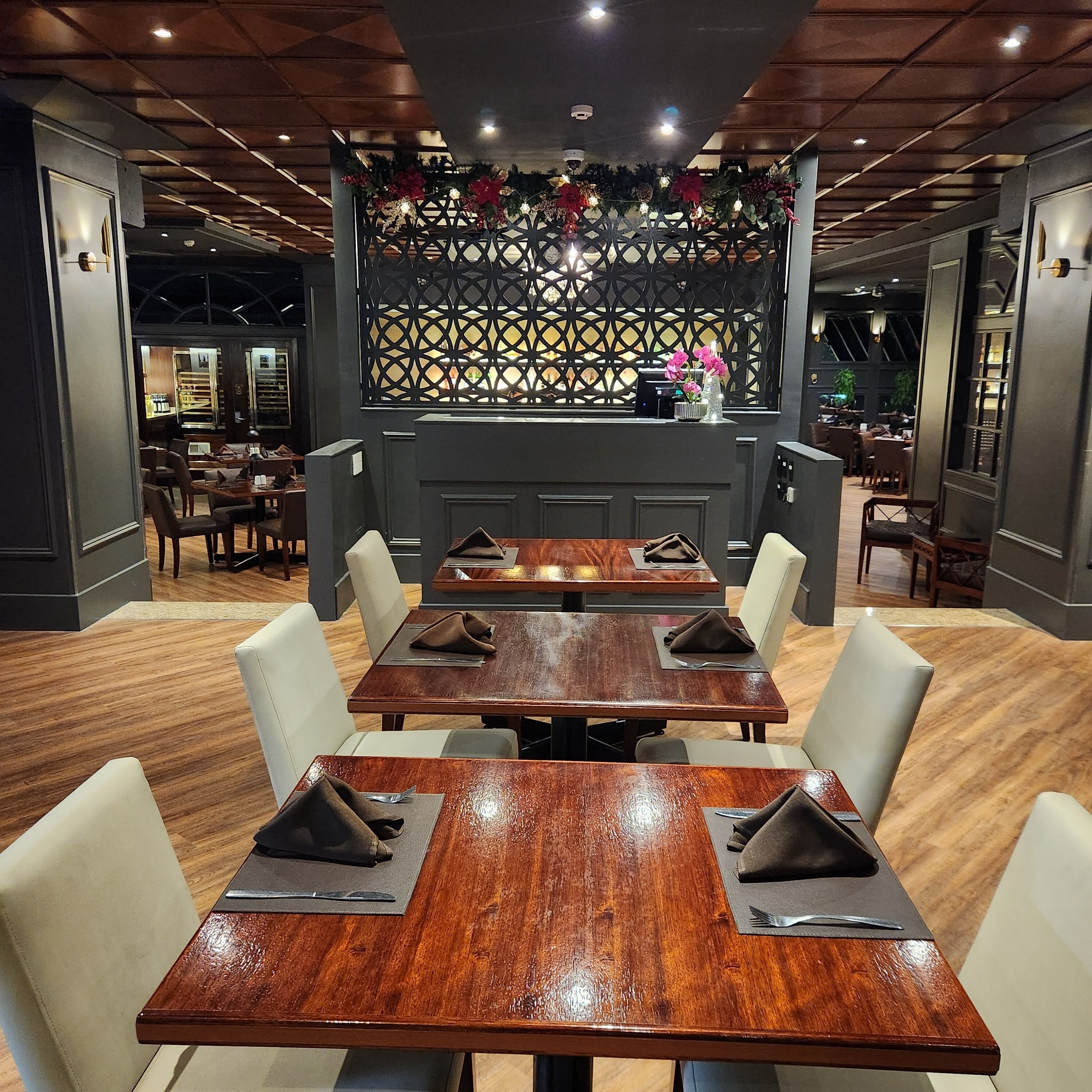 A restaurant with wooden tables and chairs, a decorative partition with lights, and a modern ceiling design.