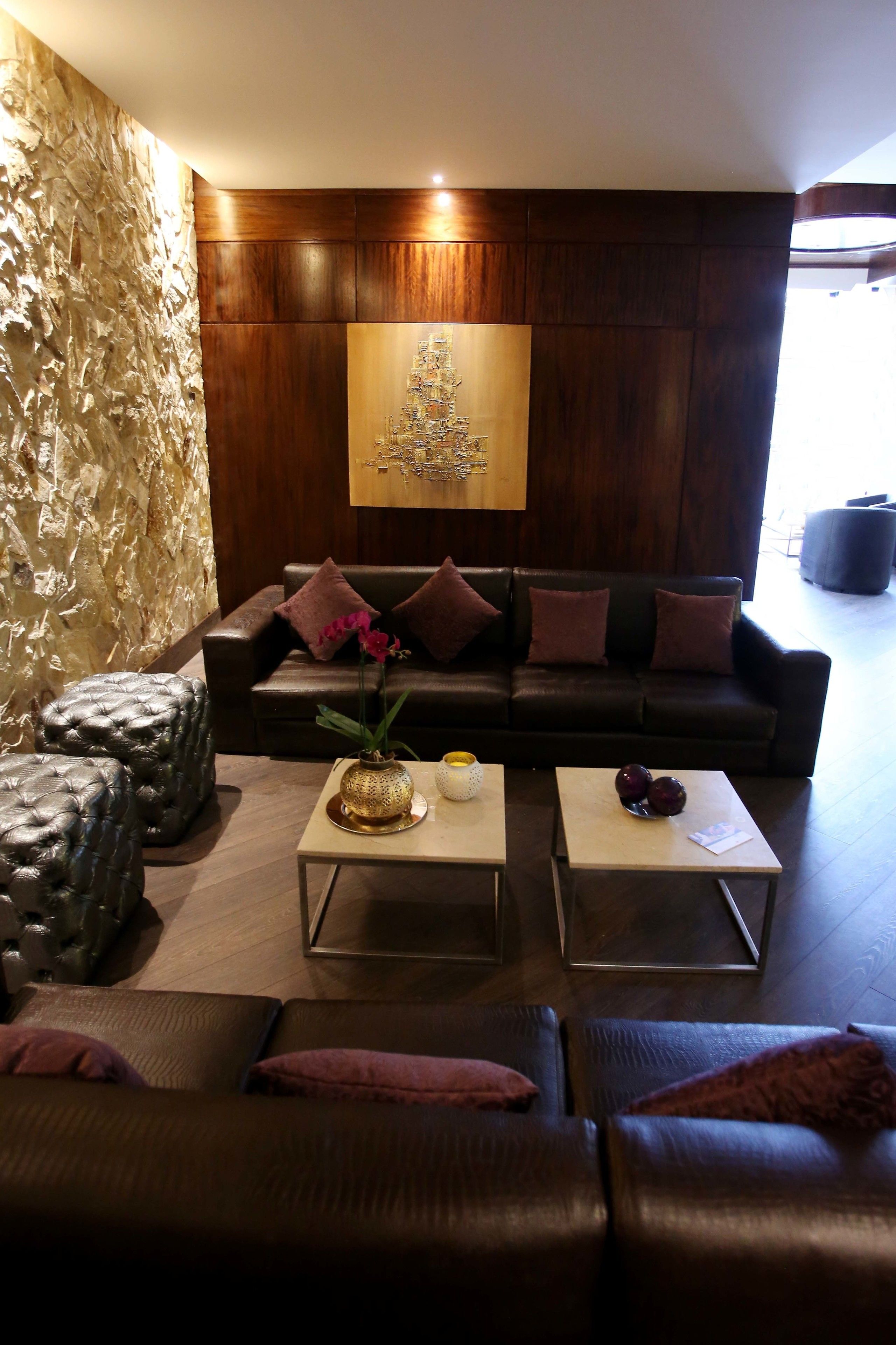 A modern living room with a dark leather sofa, two side tables, and a decorative wall piece.