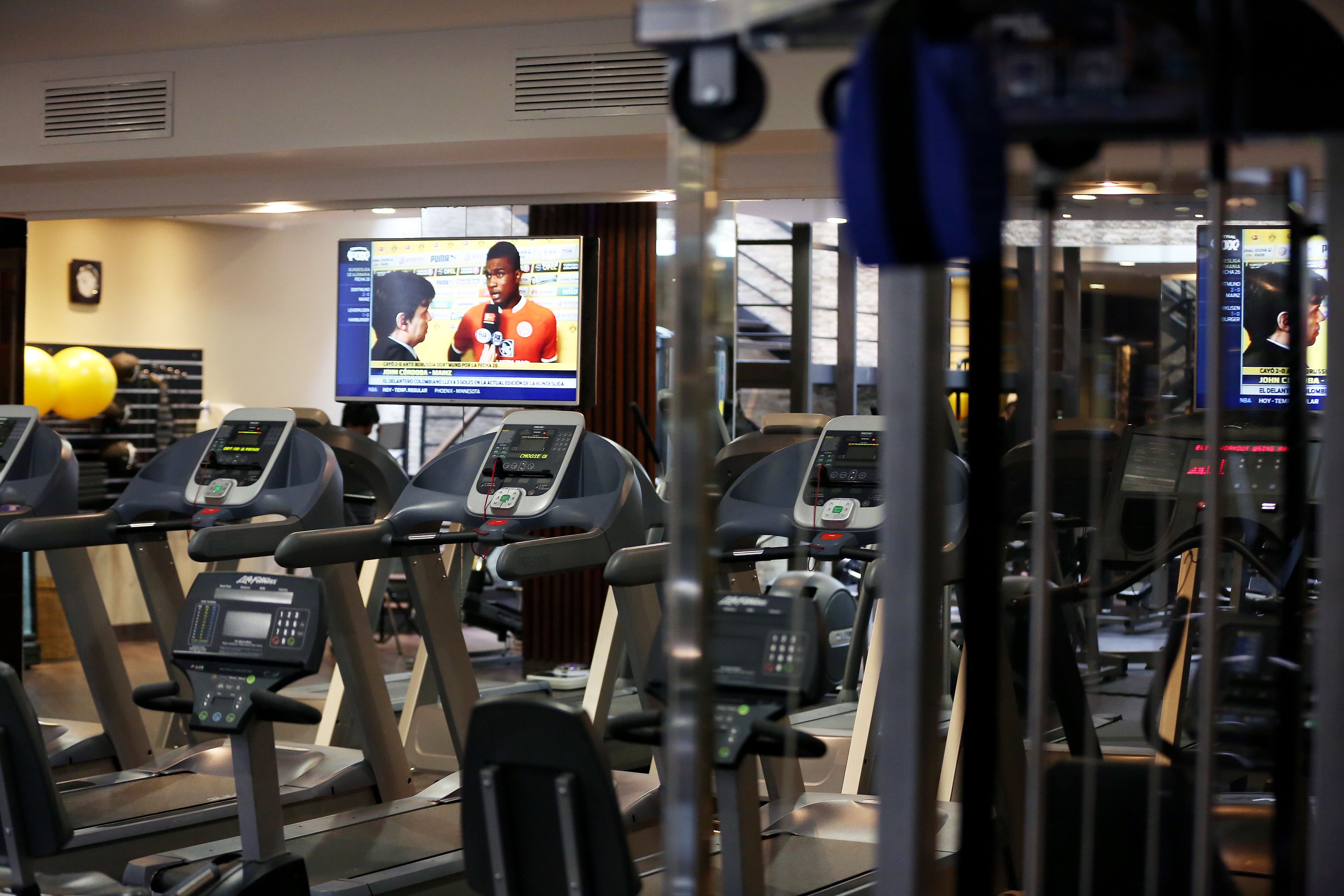 A gym with treadmills, exercise equipment, and a television displaying a news program.