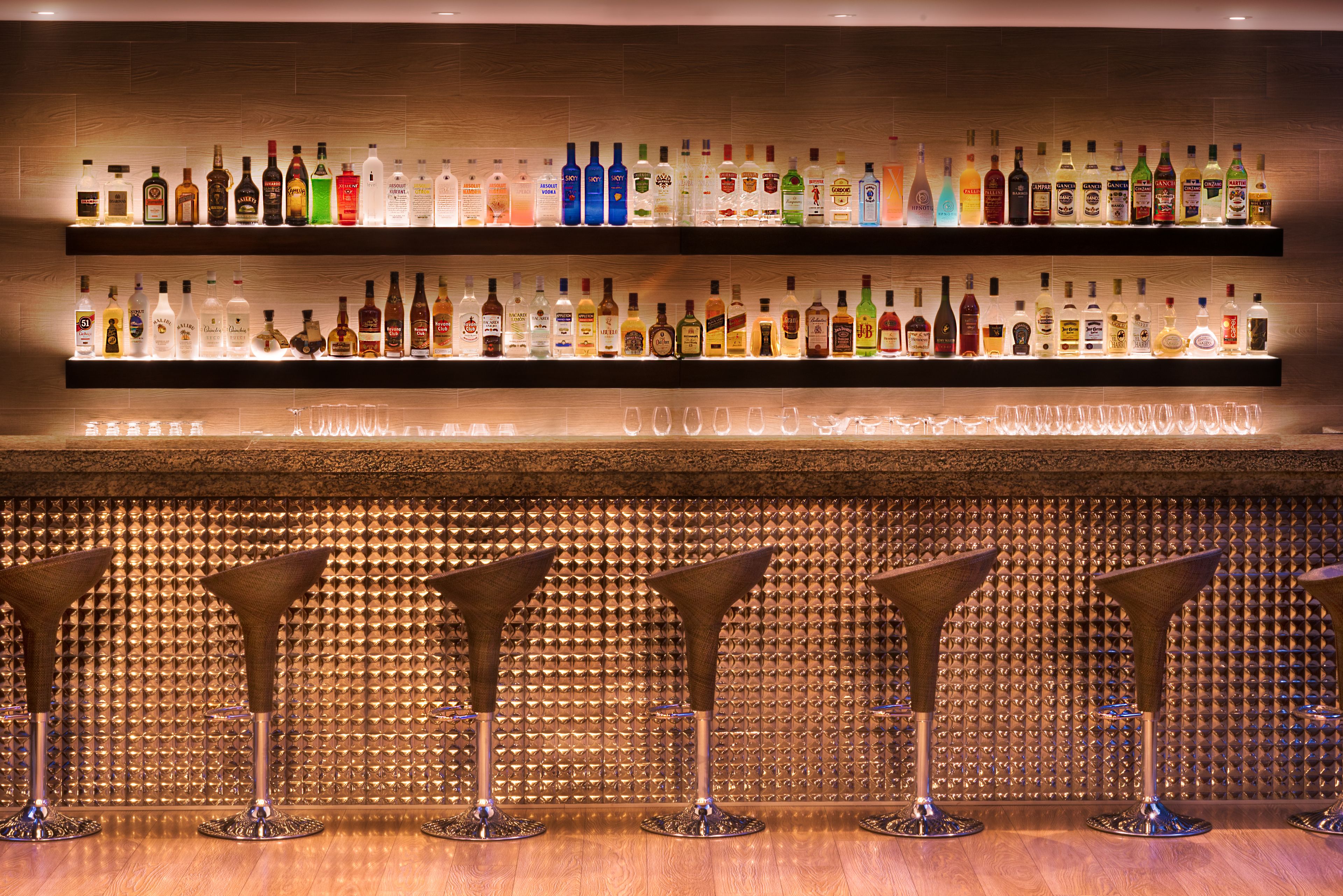 Eine Bar mit mehreren Regalen voller Spirituosenflaschen und vier Barhocker.