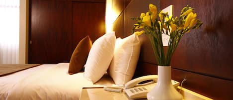 Una habitación de hotel con una cama, una mesita de noche con un teléfono y un jarrón con flores, y un cabecero de madera.