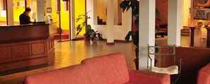 A hotel lobby with a reception desk, a red sofa, and potted plants. - Alexander Hotel (Iguazu)