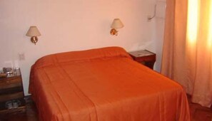 A room with a bed, two wall-mounted lamps, a nightstand, and a window with curtains.