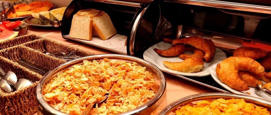 A buffet with various food items including bread, pastries, and a large serving of cereal.