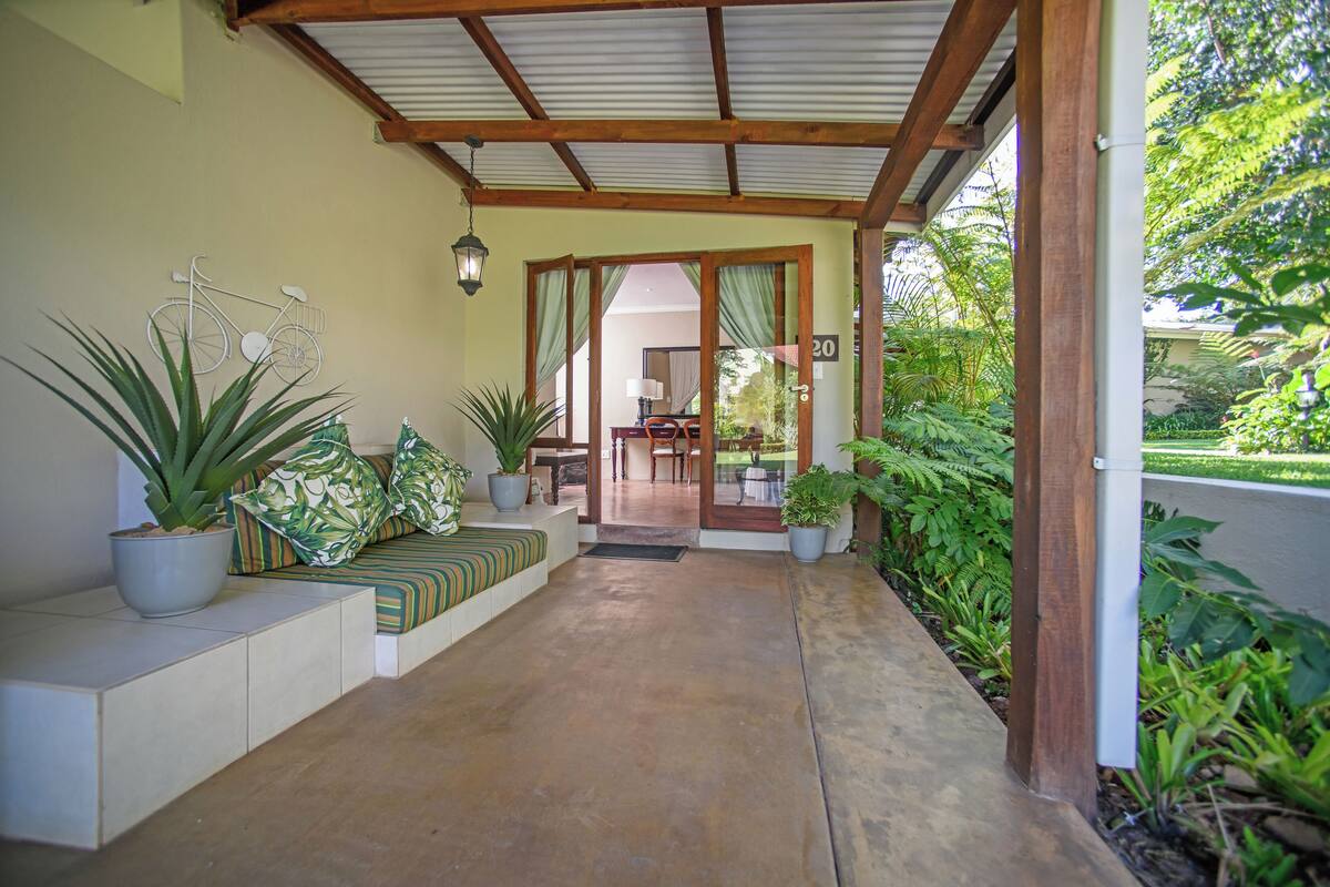 A covered outdoor area with a wooden ceiling, potted plants, and a seating area with cushions.