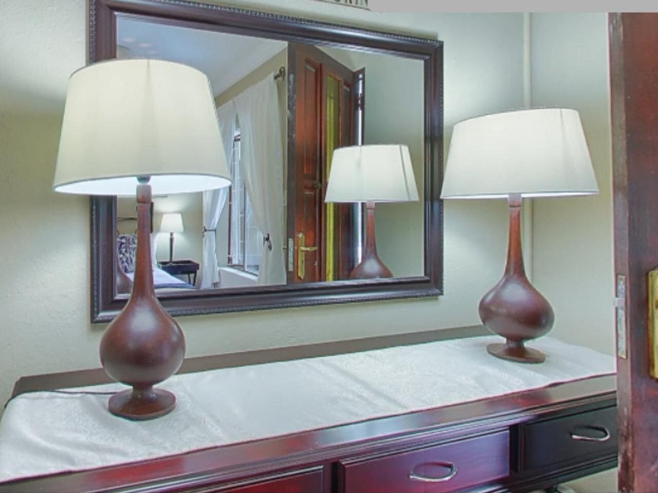 Habitación de hotel con tocador, dos lámparas, un espejo y una puerta.