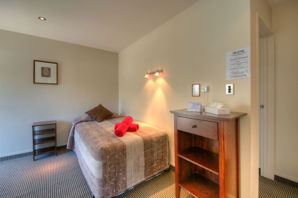 A hotel room with a bed, a bedside table with a lamp, a framed picture on the wall, and a fire action sign.