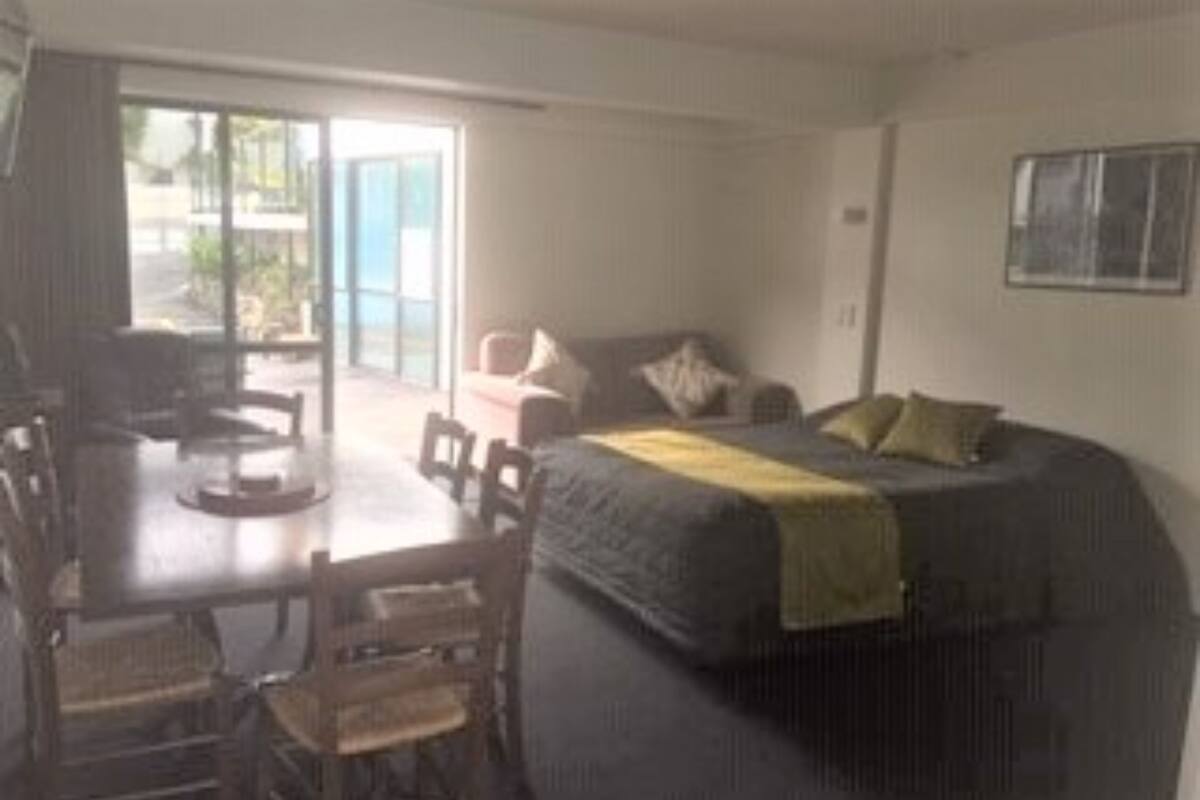 A room with a bed, a desk, and chairs. There is a window and a door leading outside.