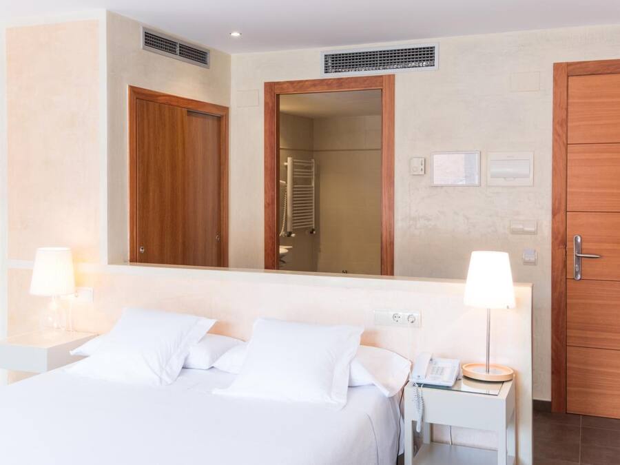 A hotel room with a bed, bedside lamps, a telephone, a mirror, and a wooden door.
