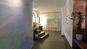 Un pasillo con una amplia pared de mármol, un mapa sobre caballetes y plantas en macetas.