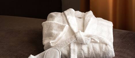 A bed with a white bathrobe and slippers on it.