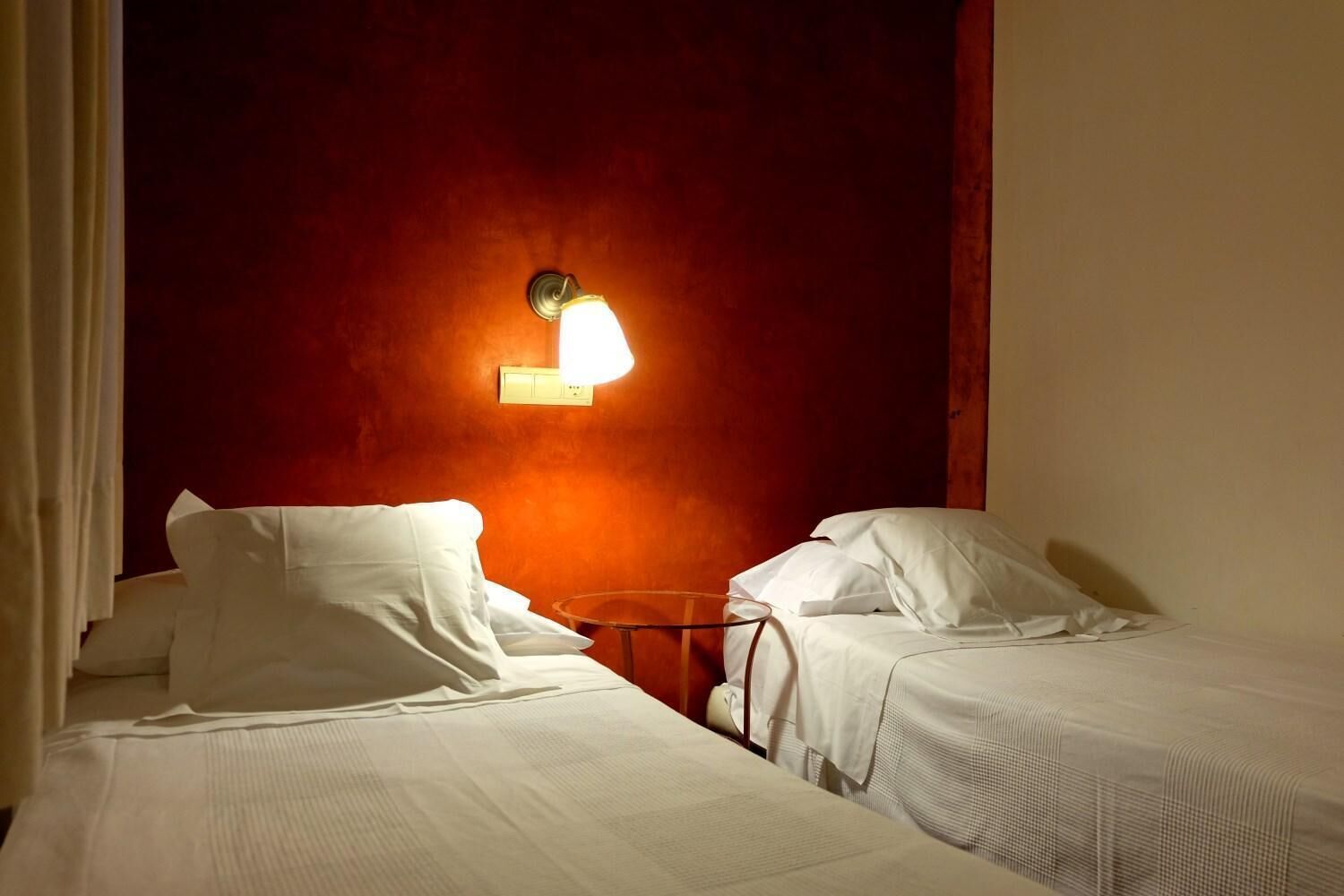 A hotel room with two single beds, a nightstand, and a wall-mounted light fixture.