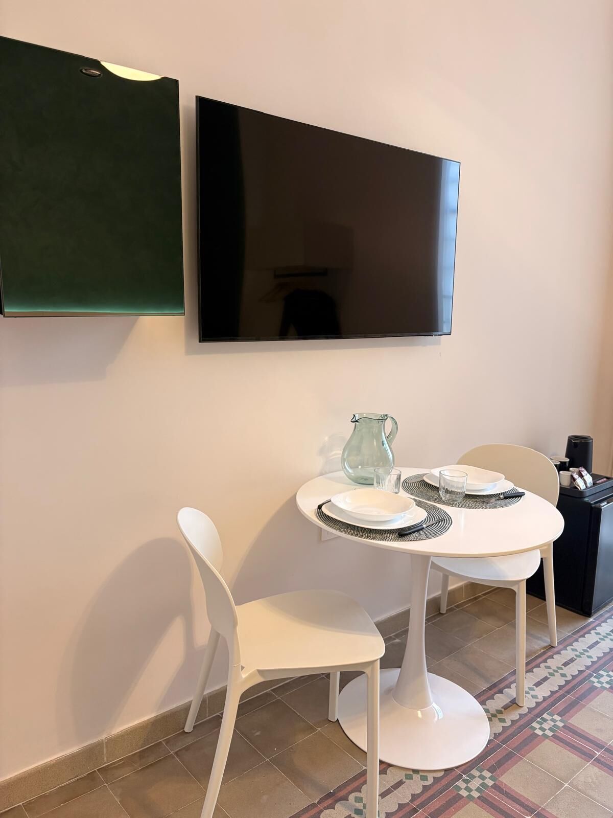 A dining area with a white table, two white chairs, a glass pitcher, and a black coffee machine.