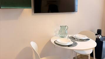 A dining area with a white table, two white chairs, a glass pitcher, and a black coffee machine.