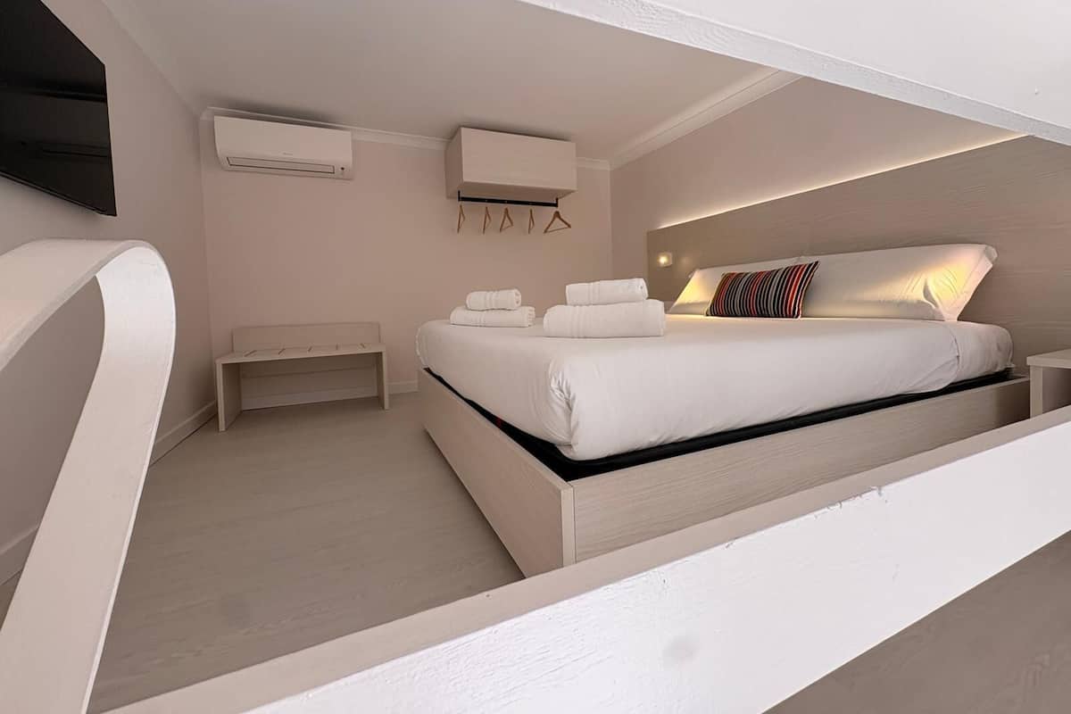 A modern bedroom with a bed, bedside tables, an air conditioning unit, and a wall-mounted TV.