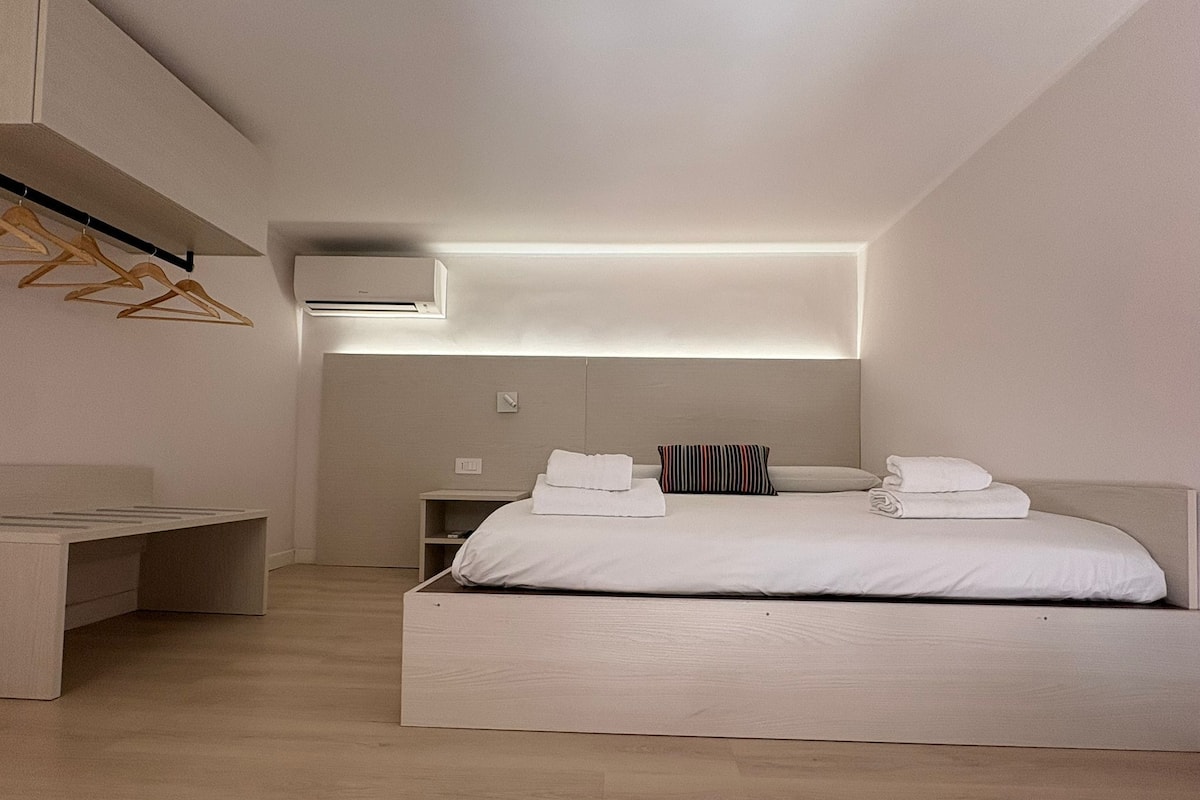A modern bedroom with a bed, bedside tables, a hanging wardrobe, and a built-in air conditioning unit.