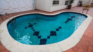 A swimming pool with a tiled edge, a white wall with a geometric pattern, and a potted plant. - Gardenia Hotel (Amman)