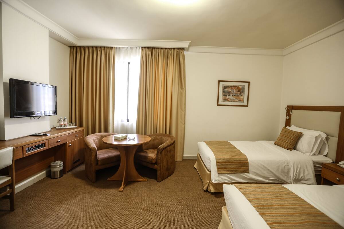 A hotel room with a bed, a desk with a television, a chair, and a small table.
