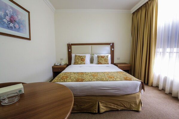 Un cuarto de hotel con una cama grande, una mesita de noche, una mesa redonda y un cuadro en la pared.