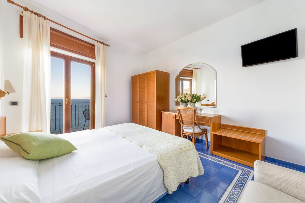 Ein Hotelzimmer mit Bett, Schreibtisch, Stuhl, Kleiderschrank, Spiegel und Fernseher.