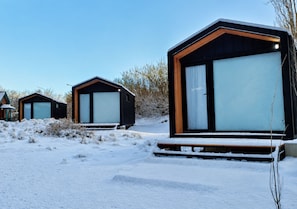 En modern stuga med stora fönster, en träveranda och ett snötäckt landskap.