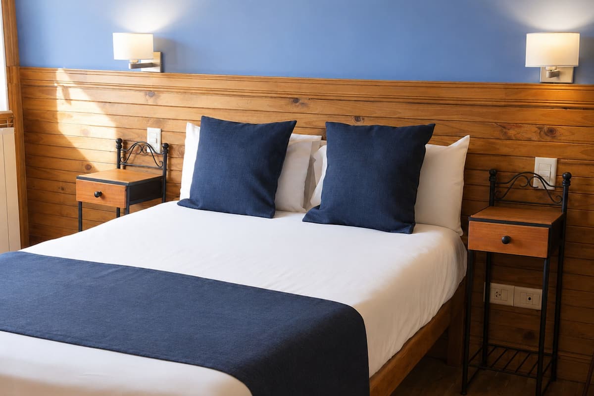 Una cama con cabecera de madera, dos mesitas de noche y lámparas fijadas a la pared.