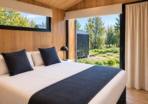 A bedroom with a large bed, wooden walls, a window with curtains, and a view of greenery outside. - Hainen by DOT Tradition (El Calafate)