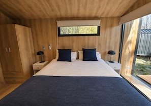 A bedroom with a large bed, two bedside tables, a window, and wooden walls. - Hosteria Hainen (El Calafate)