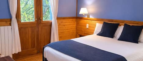 A bedroom with a wooden headboard, a bed with white and dark blue bedding, a bedside table, and a window with curtains.