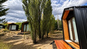 Moderne buitenaccommodatie met houten terrasstoelen, een zwarte gevel en een natuurlijke omgeving.