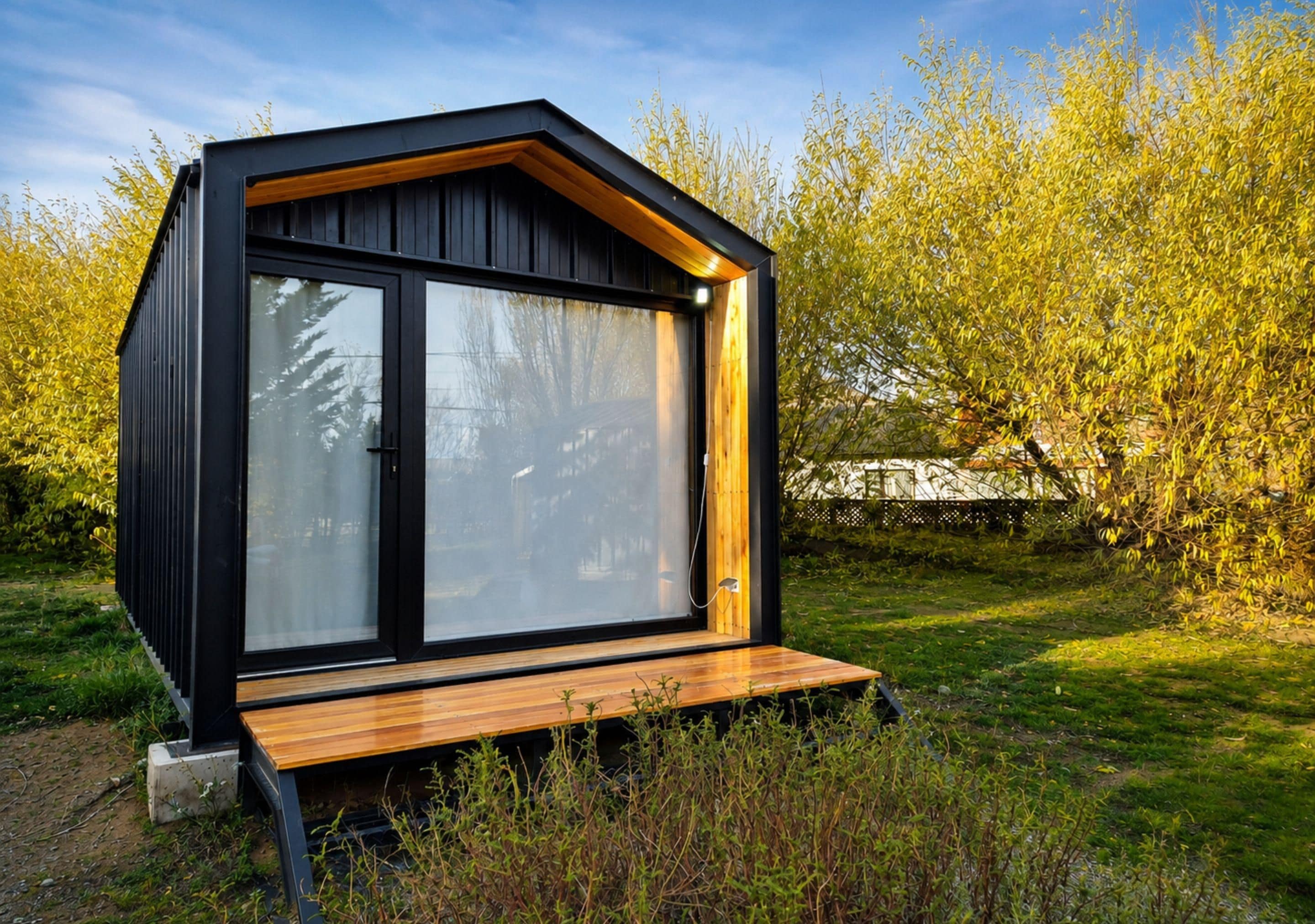 A modern, compact cabin with a large sliding glass door, a wooden deck, and a surrounding natural landscape.