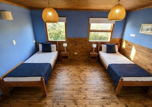 A room with two wooden beds, each with a blue bedspread and white linens, flanked by nightstands with lamps. - Hainen by DOT Tradition (El Calafate)